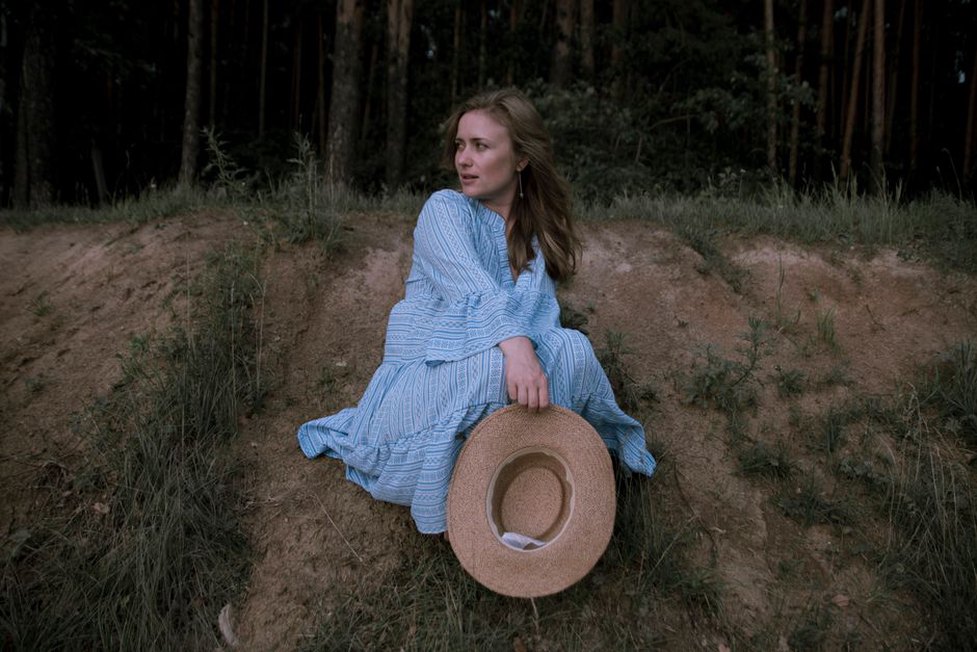 Woman in baby blue pleated maxi dress with balloon sleeves, standing in a sunlit garden