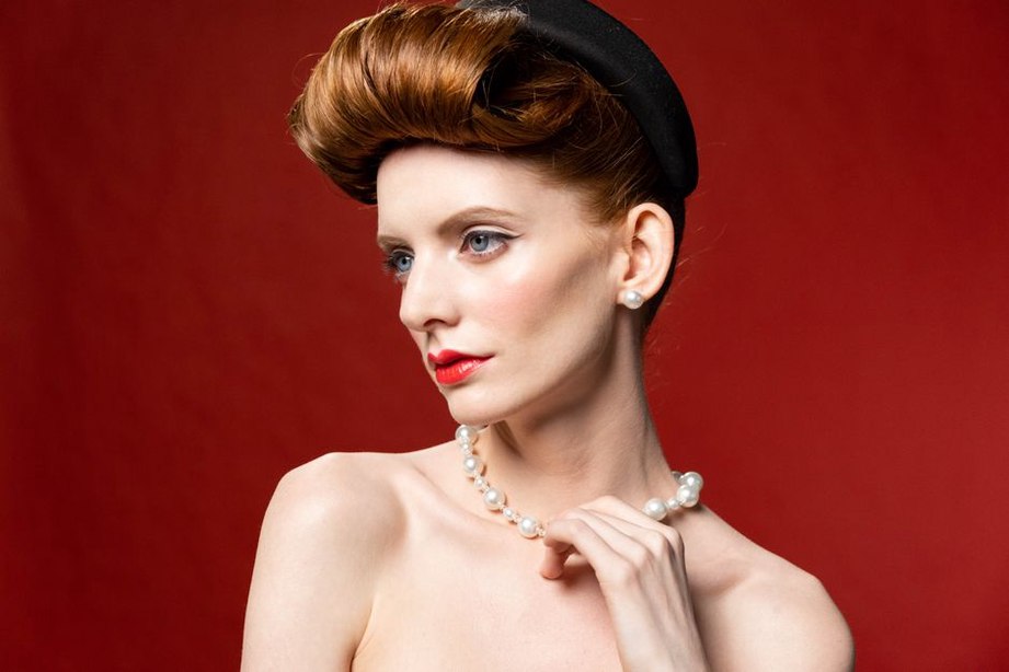 Fingers gently pushing a dark green Bakelite pin into a low chignon, 1940s style