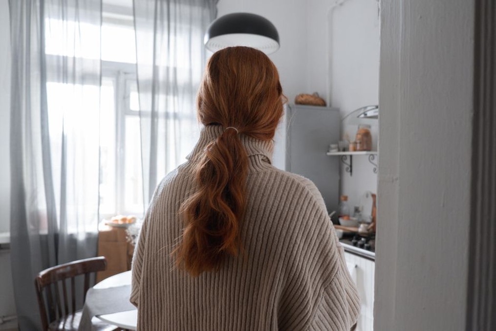 A woman with dark hair styled in a low side ponytail, secured with a burgundy velvet scrunchie, wearing a cream knit sweater