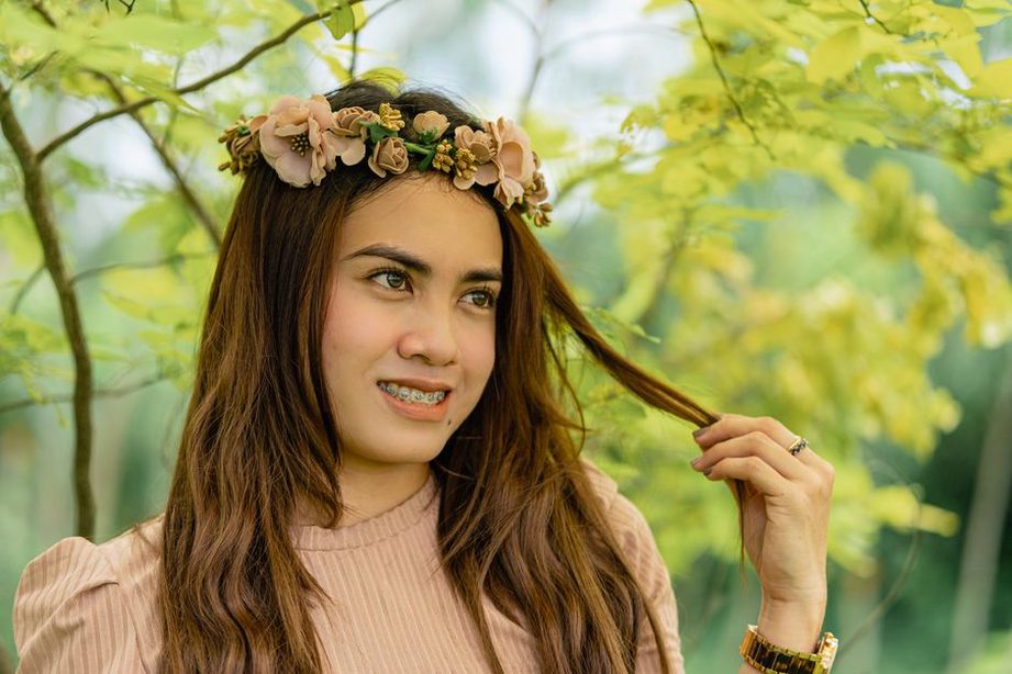 A woman in a white blouse and blue skirt poses with a rose crown headband in her hair