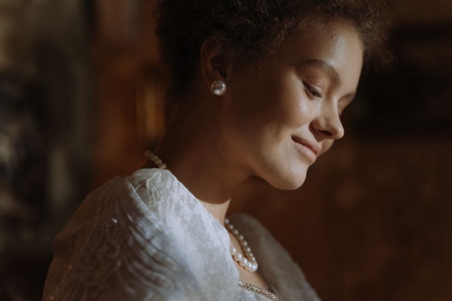 Side view of a woman with a low bun secured by a gold pearl barrette, wearing a white blouse