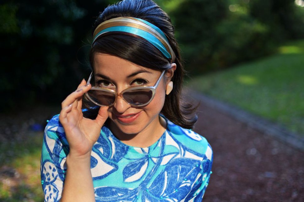 A woman in a cream blouse and blue jeans, a pastel green ric rac headband holding back her hair