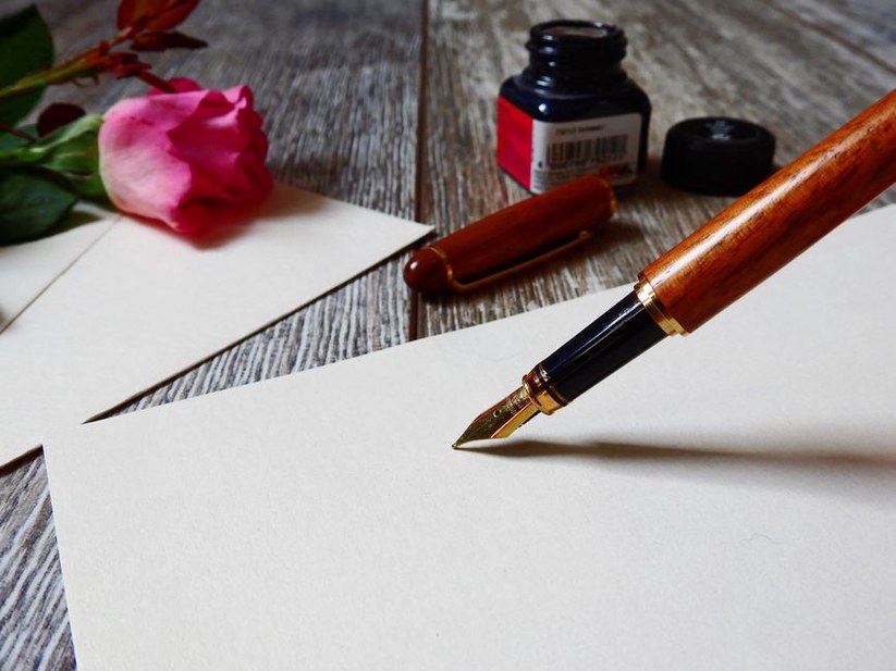 writer at wooden desk with fountain pen and stationery